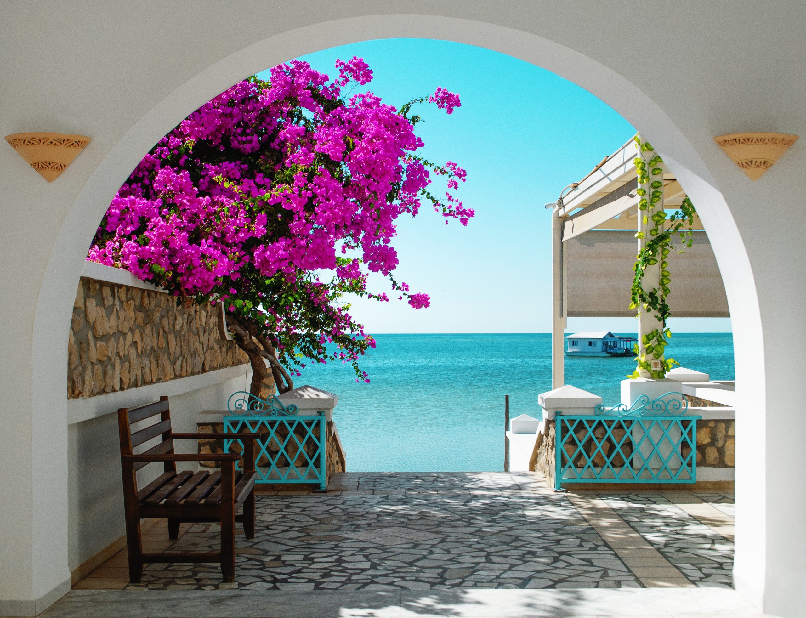 view blue sea tunisia through white archway with pink blooming flowers foreground distance house water scaled
